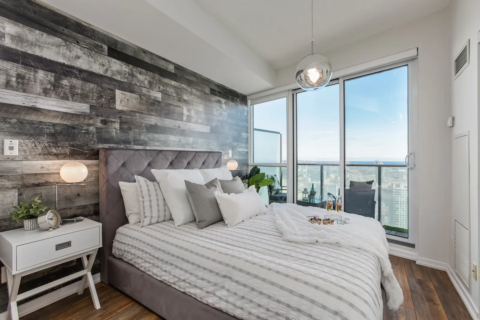 Interior of a waterfront condo in Toronto, with a grey sofa, a light kitchen, and a view of the lake.
