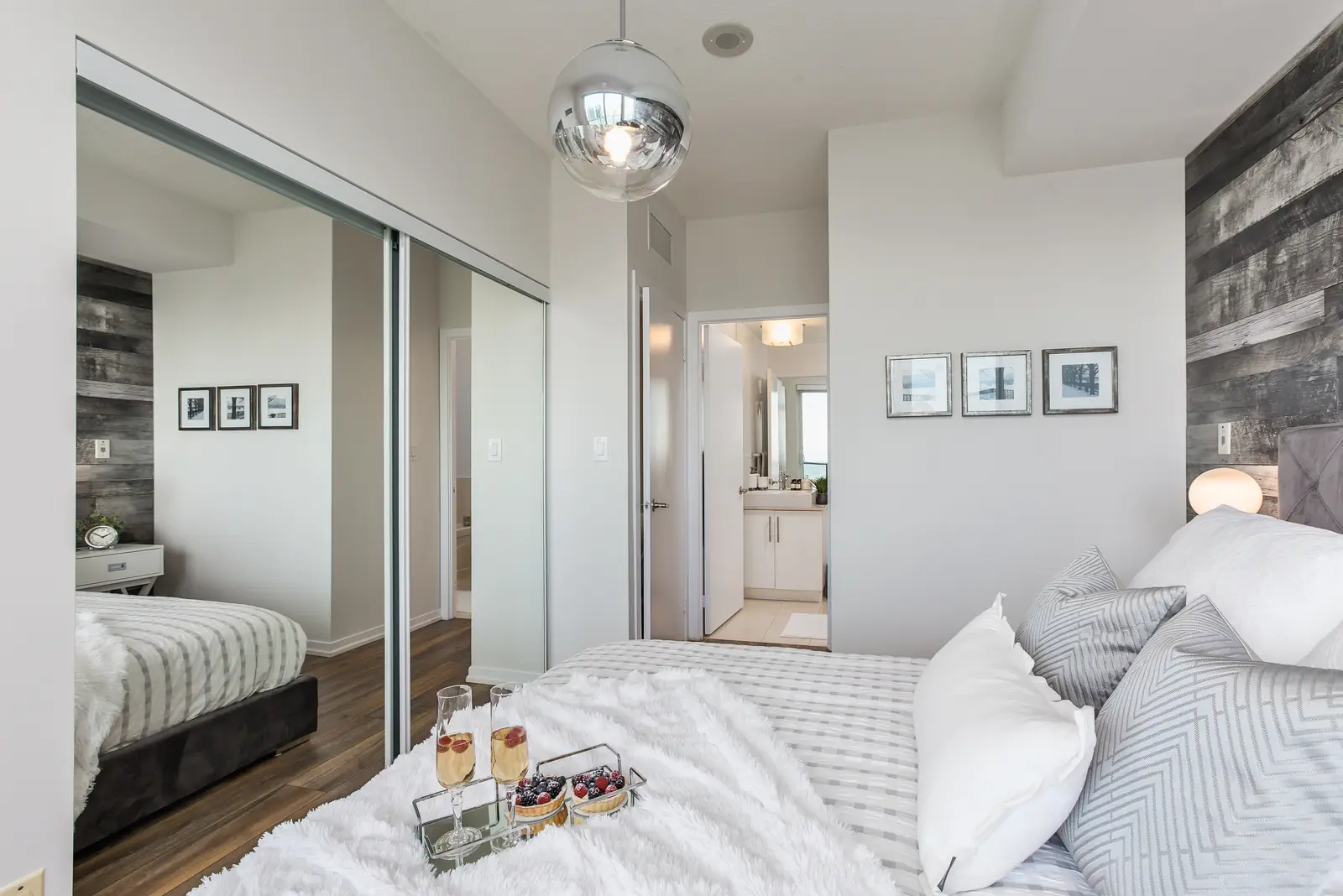 Interior of a waterfront condo in Toronto, with a grey sofa, a light kitchen, and a view of the lake.