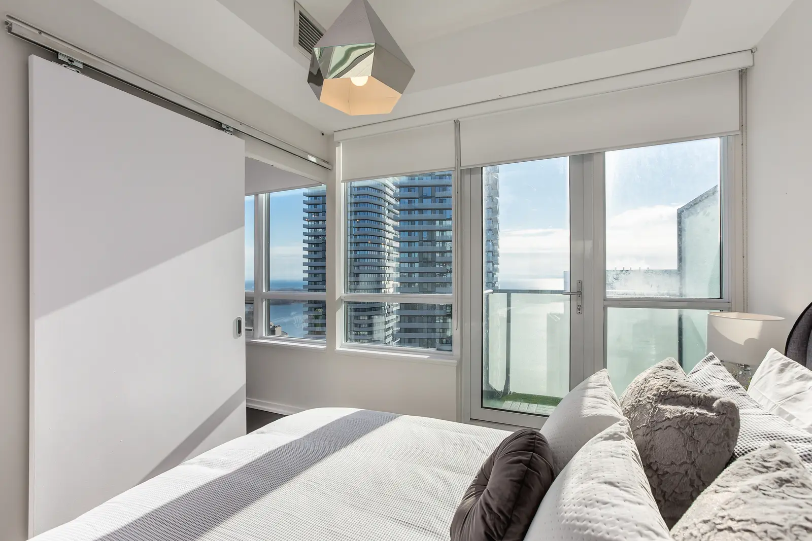 Interior of a waterfront condo in Toronto, with a grey sofa, a light kitchen, and a view of the lake.