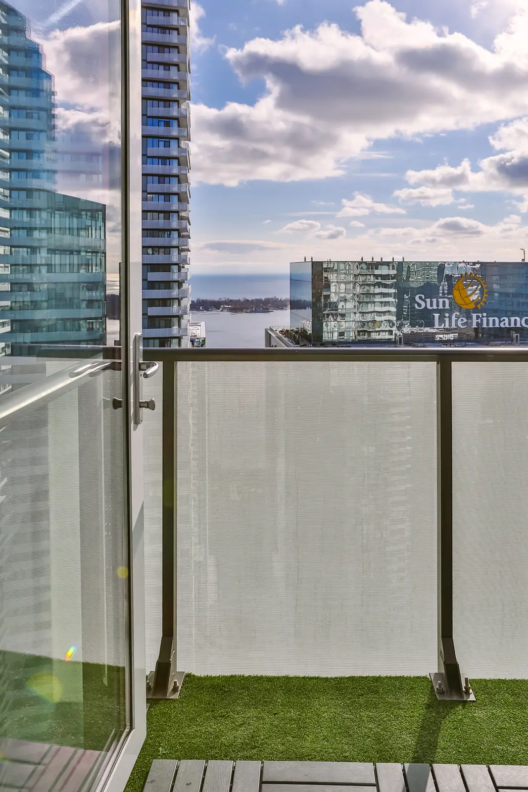 Interior of a waterfront condo in Toronto, with a grey sofa, a light kitchen, and a view of the lake.