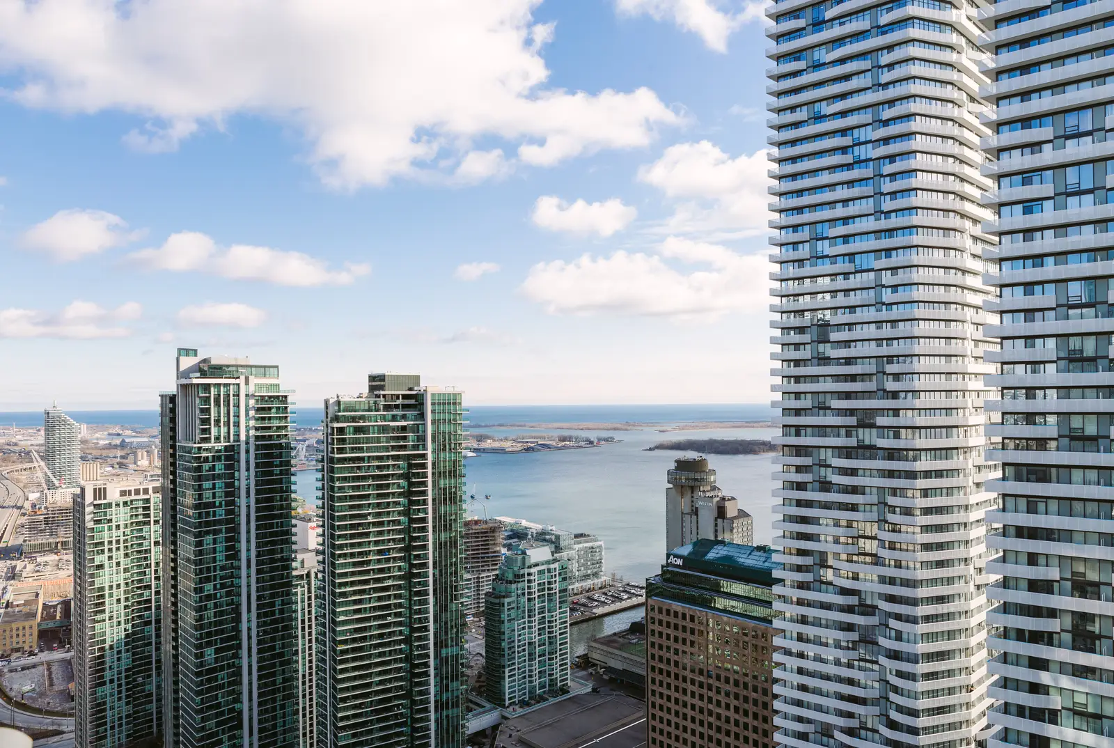 Interior of a waterfront condo in Toronto, with a grey sofa, a light kitchen, and a view of the lake.