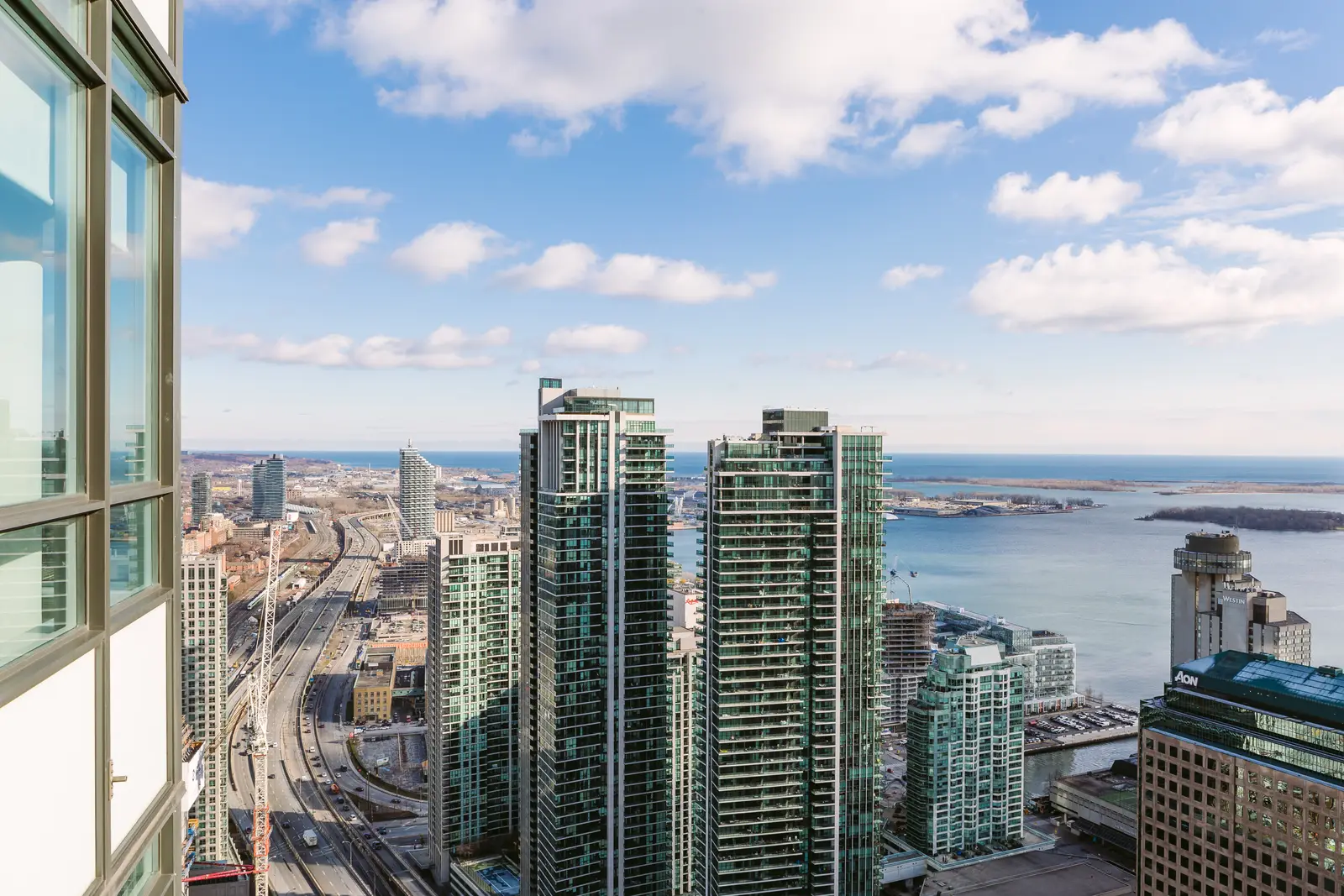 Interior of a waterfront condo in Toronto, with a grey sofa, a light kitchen, and a view of the lake.
