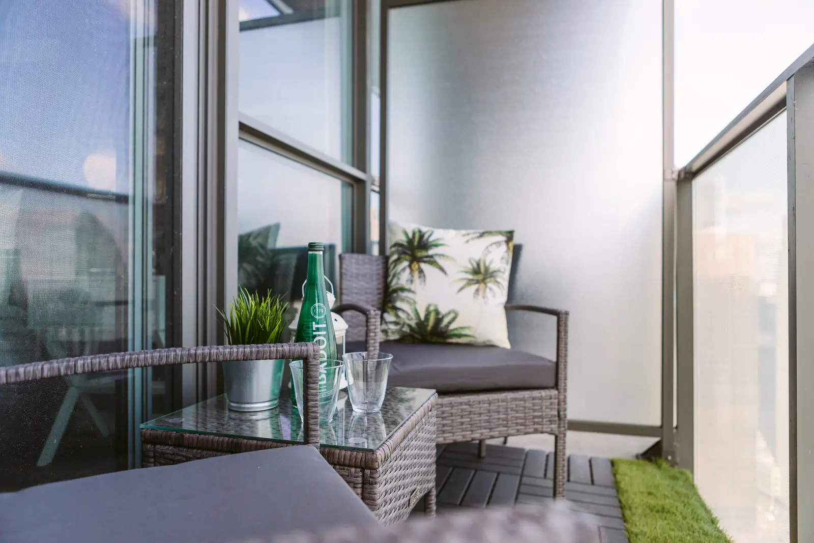 Interior of a waterfront condo in Toronto, with a grey sofa, a light kitchen, and a view of the lake.