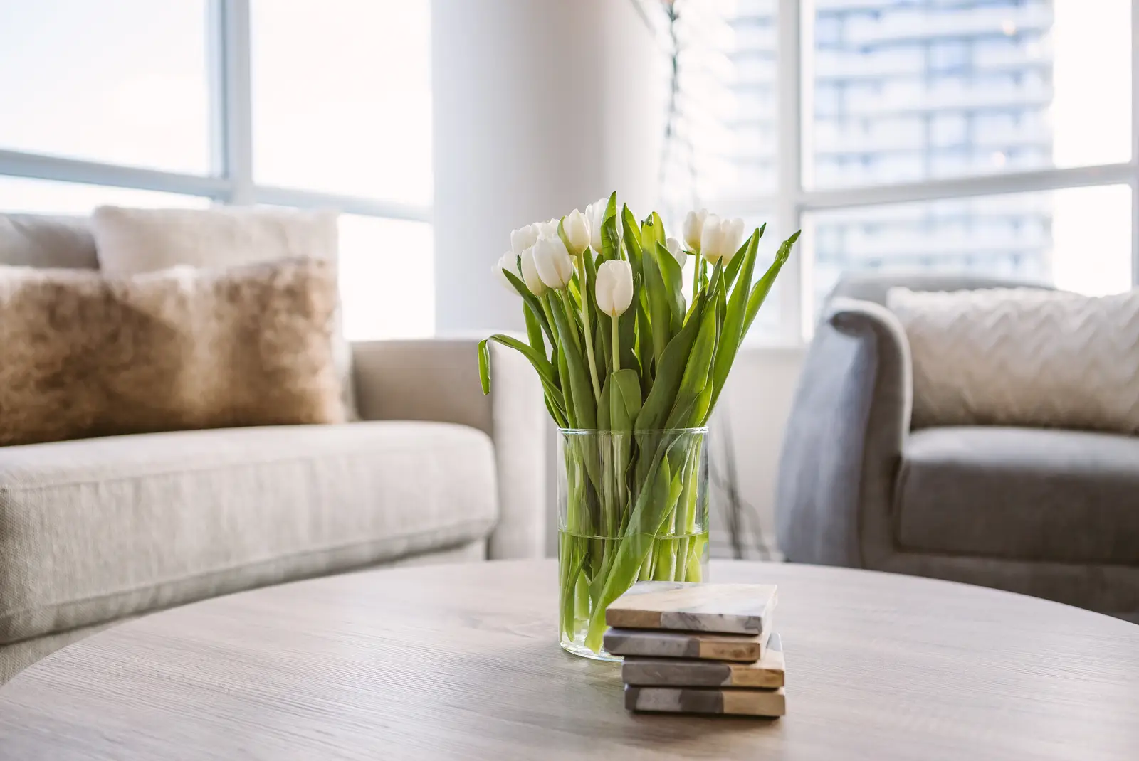 Interior of a waterfront condo in Toronto, with a grey sofa, a light kitchen, and a view of the lake.