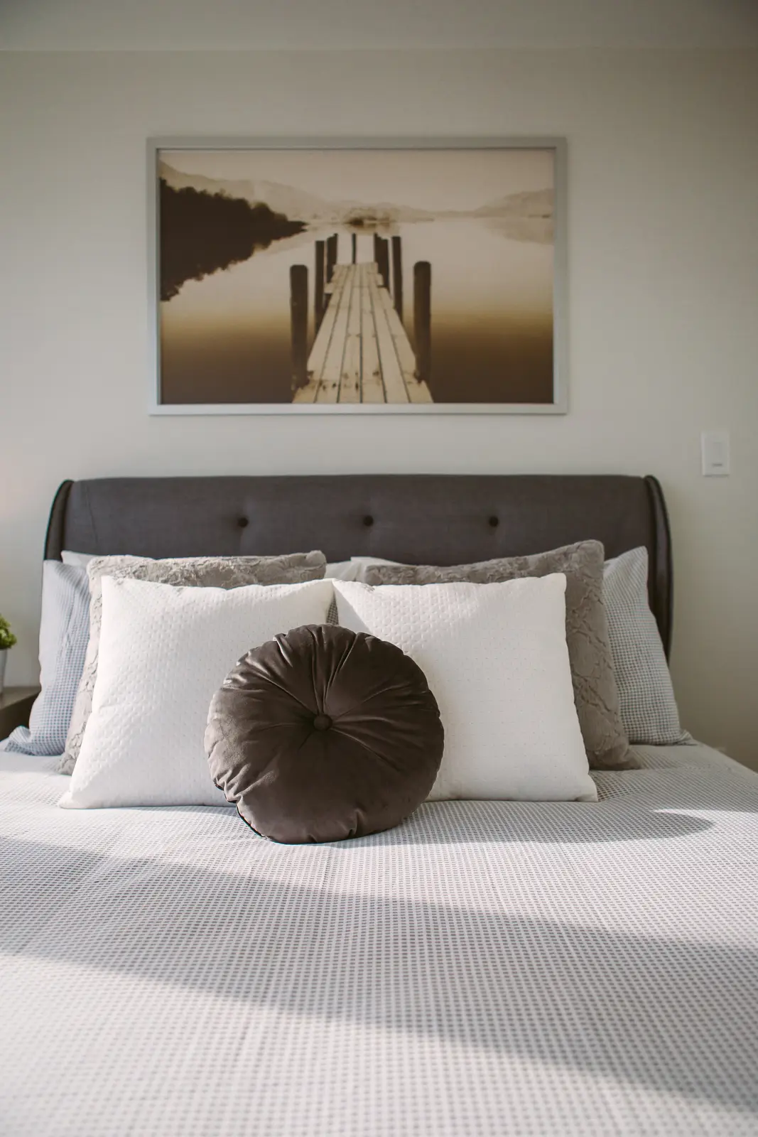 Interior of a waterfront condo in Toronto, with a grey sofa, a light kitchen, and a view of the lake.