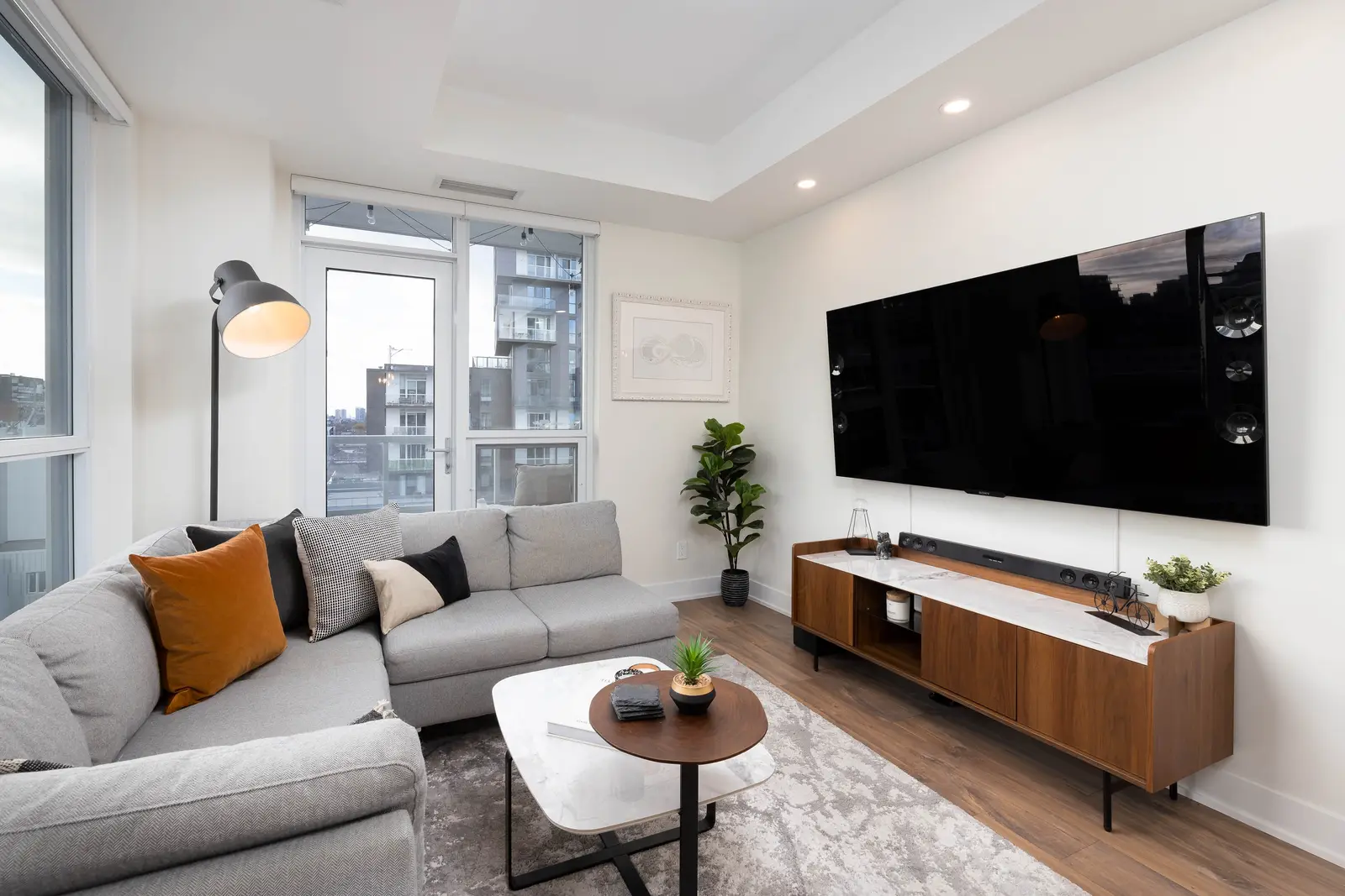 Interior of a Queen West condo in Toronto, with a grey sectional, a white kitchen, and black counters.