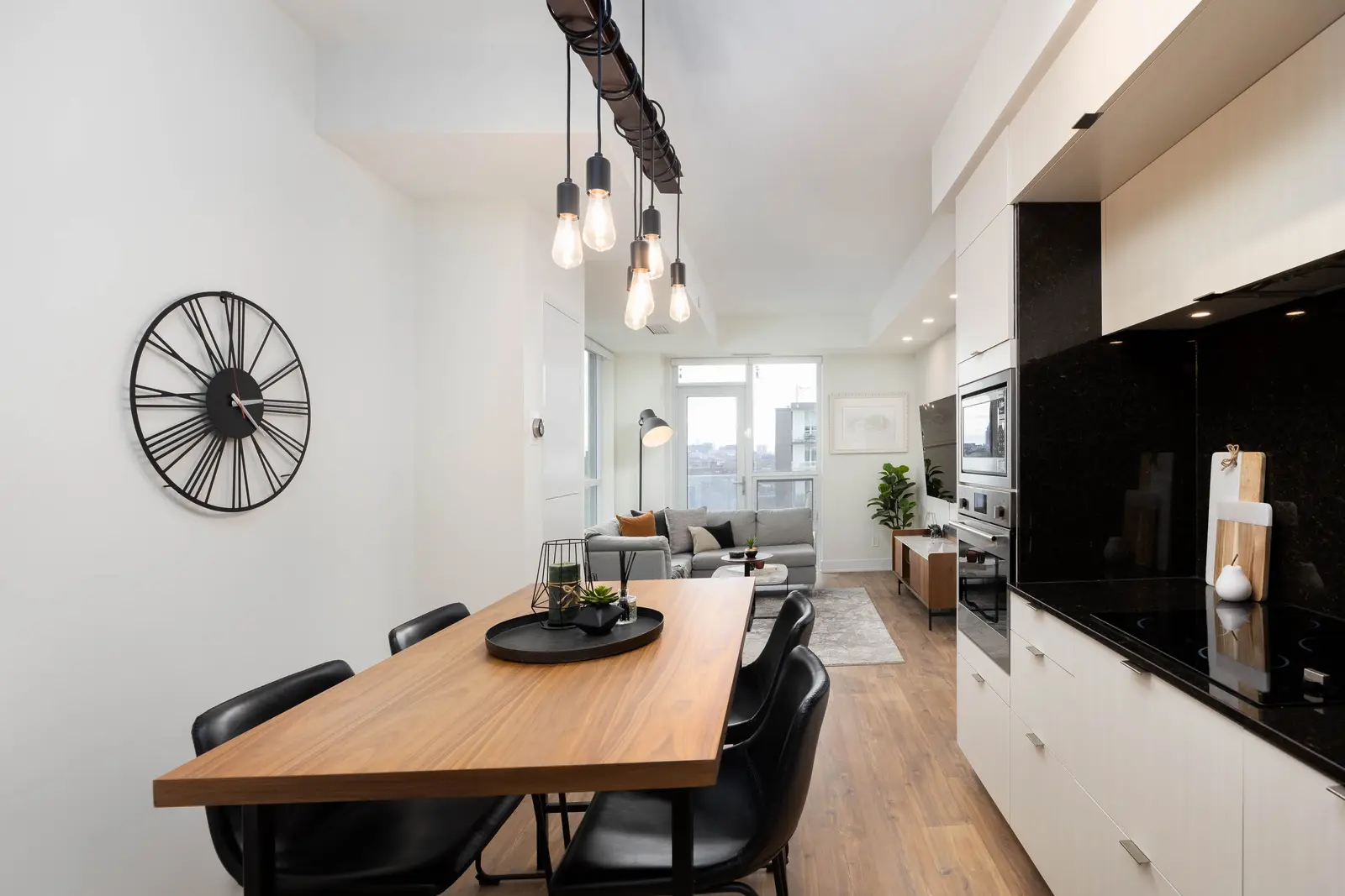 Interior of a Queen West condo in Toronto, with a grey sectional, a white kitchen, and black counters.