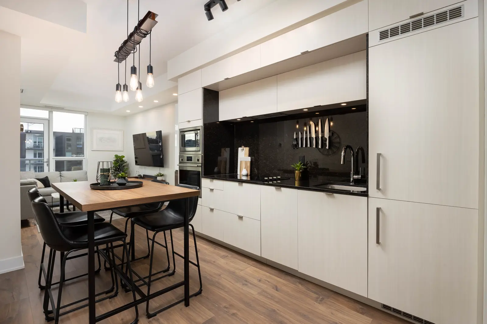 Interior of a Queen West condo in Toronto, with a grey sectional, a white kitchen, and black counters.