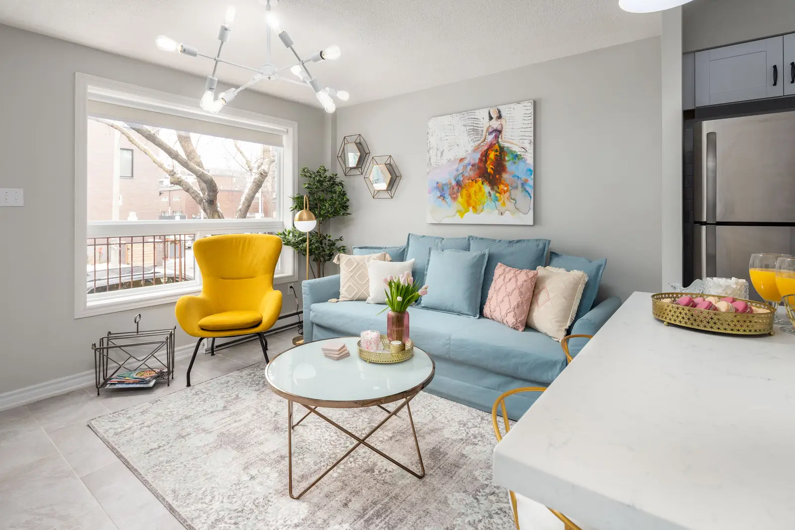 Interior of an apartment on Clinton Street in Toronto, with a blue sofa, a yellow chair, and a white kitchen.