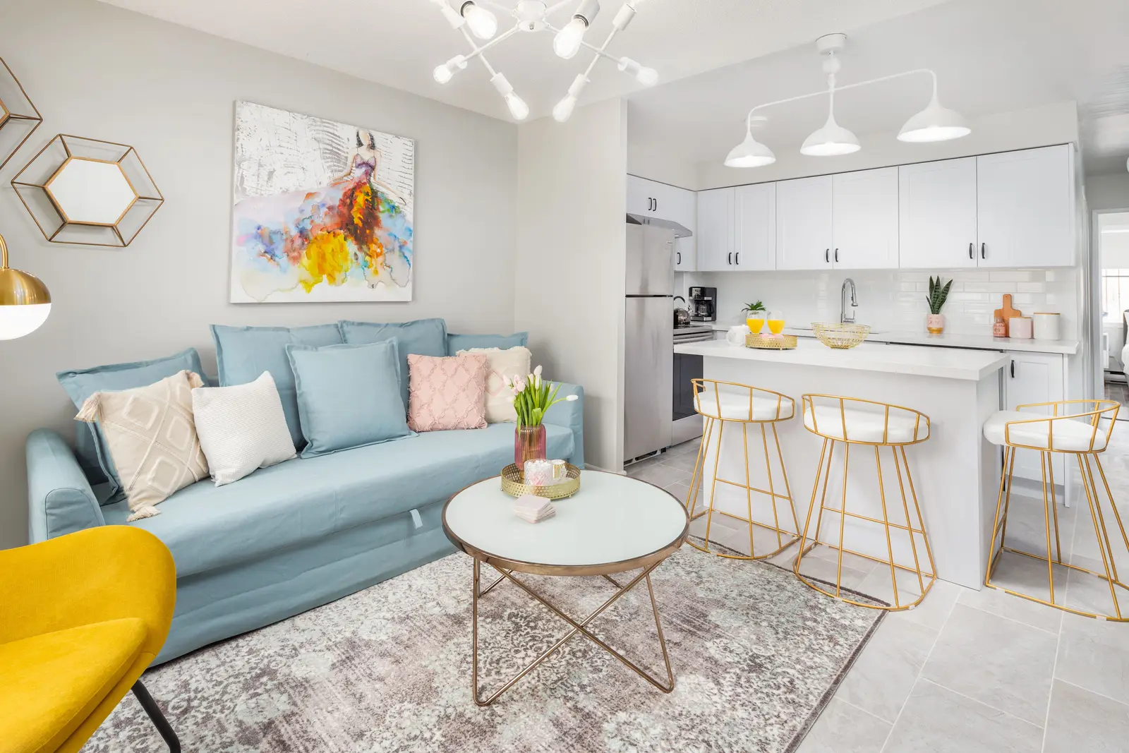 Interior of an apartment on Clinton Street in Toronto, with a blue sofa, a yellow chair, and a white kitchen.