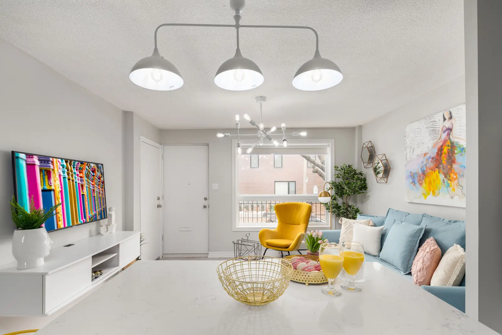 Interior of an apartment on Clinton Street in Toronto, with a blue sofa, a yellow chair, and a white kitchen.