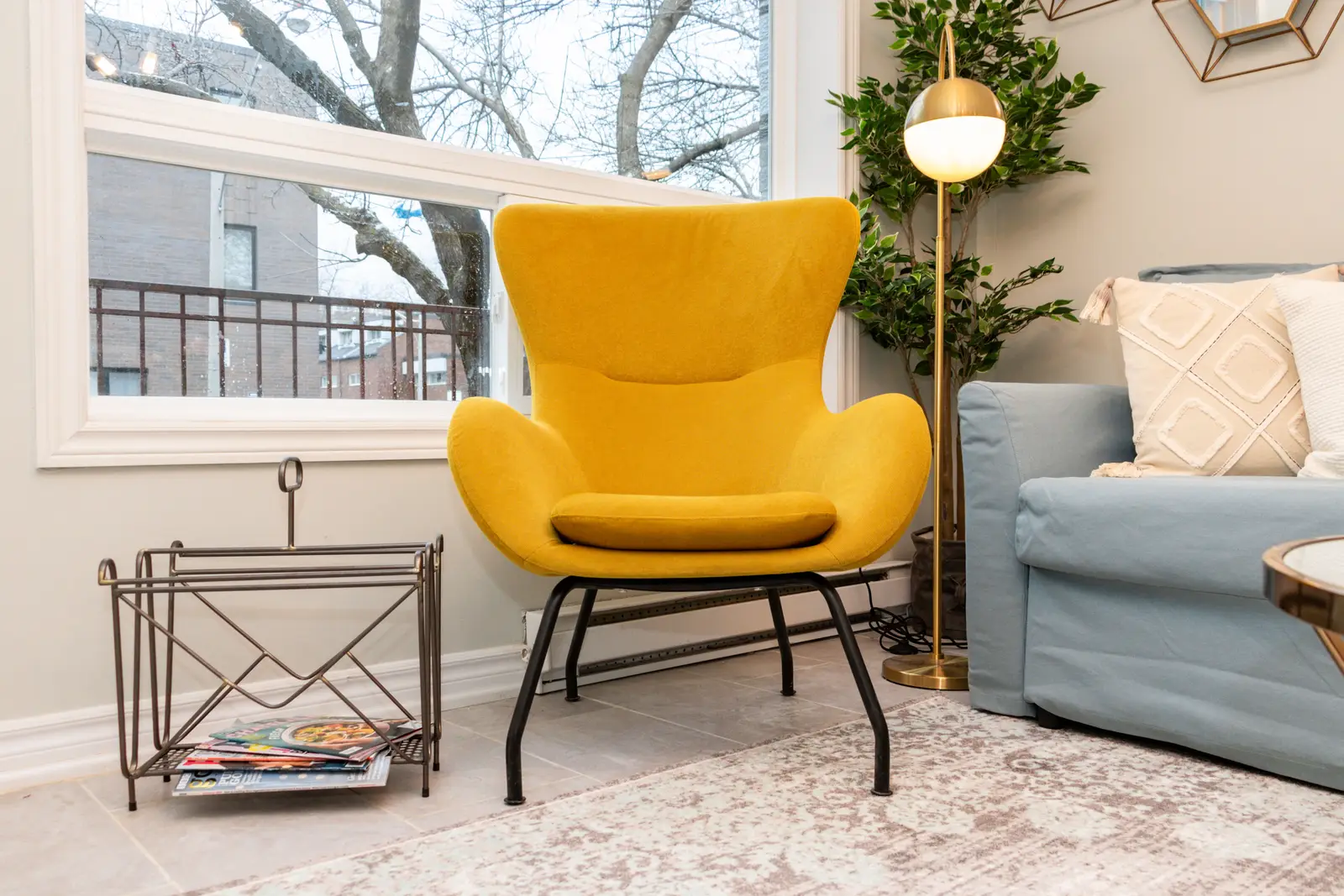 Interior of an apartment on Clinton Street in Toronto, with a blue sofa, a yellow chair, and a white kitchen.