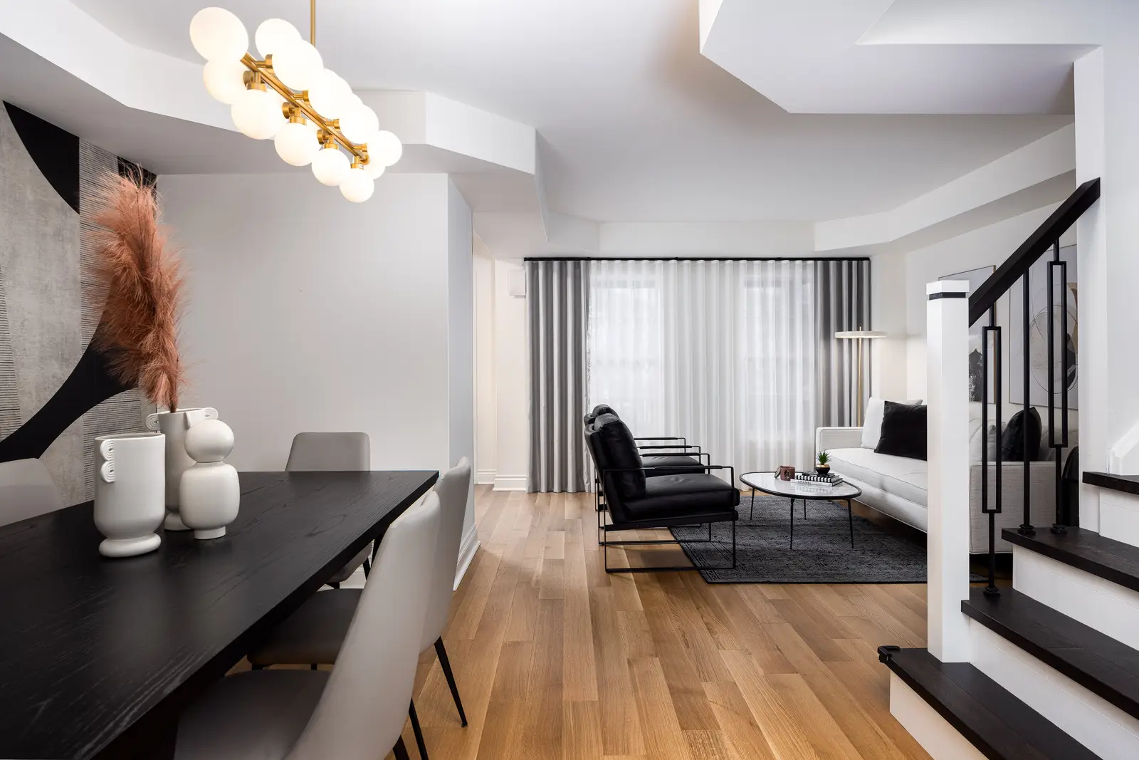 Interior of an Oakville house, with a dark dining table, light wood floors, and a white living room.