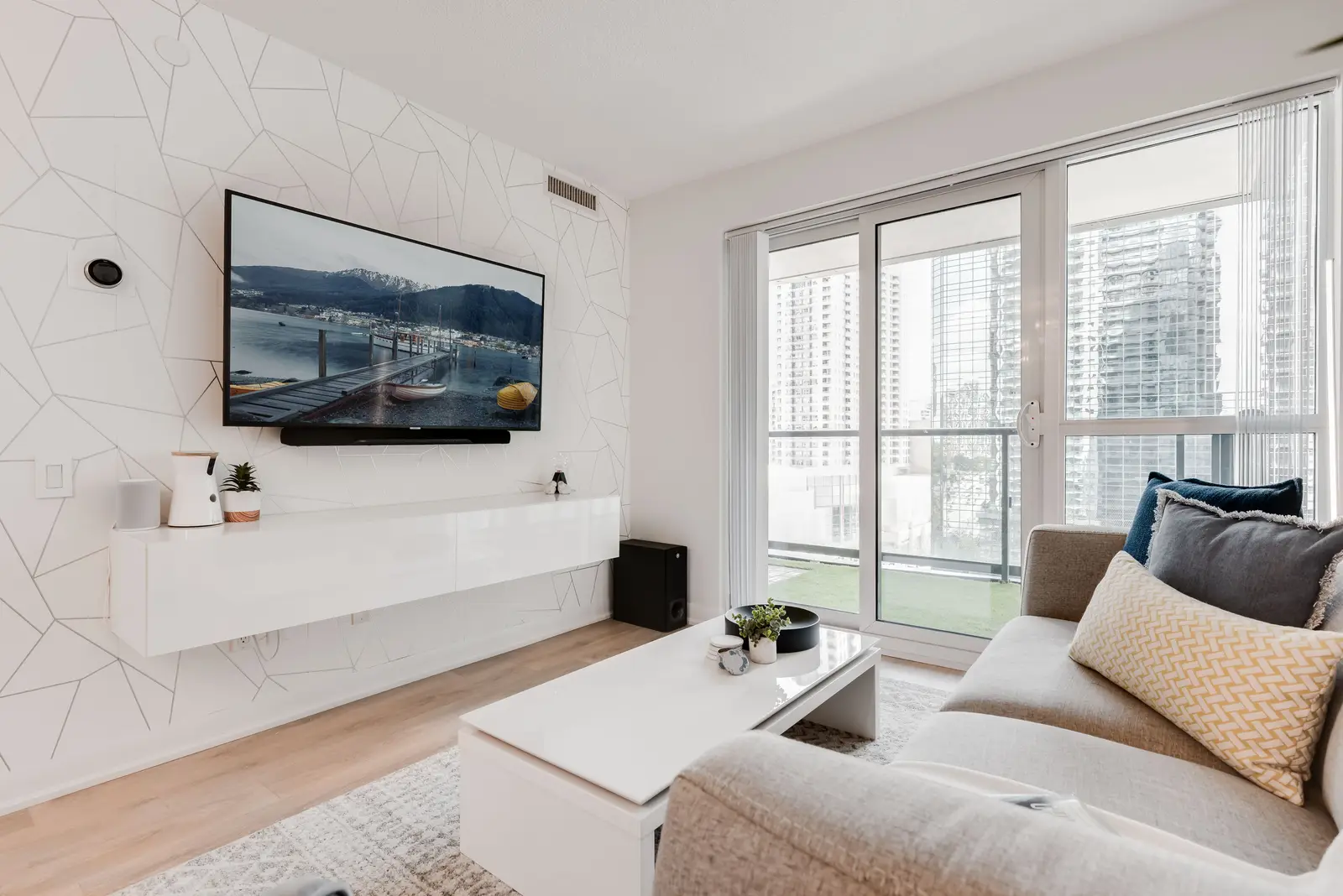 Interior of a North York condo, with a pale sofa, a white kitchen, and light wood floors.