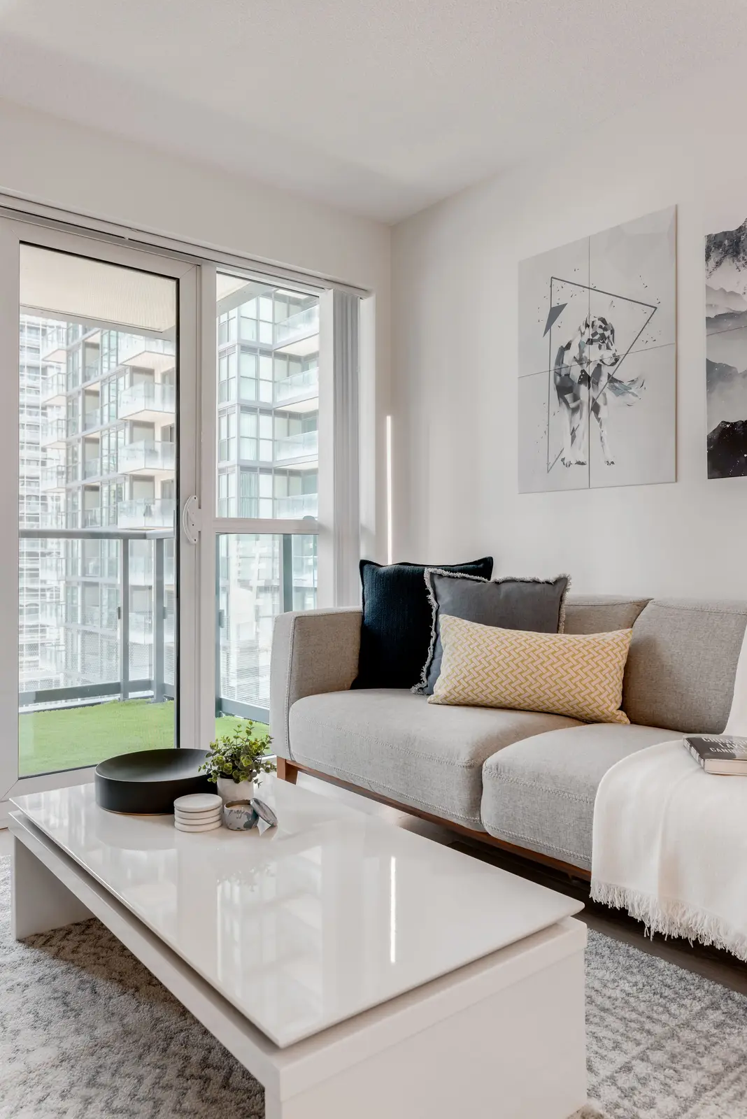 Interior of a North York condo, with a pale sofa, a white kitchen, and light wood floors.