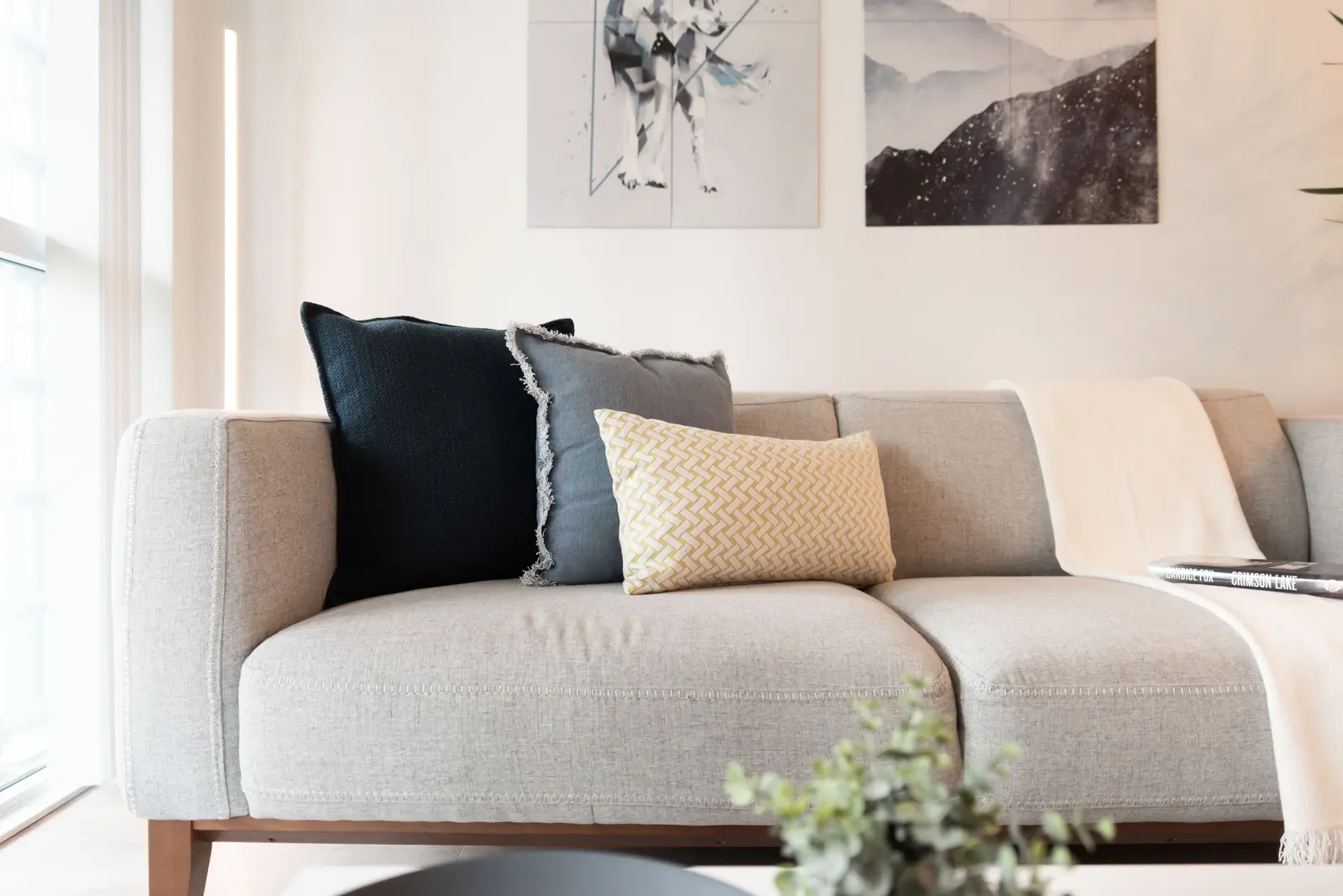 Interior of a North York condo, with a pale sofa, a white kitchen, and light wood floors.