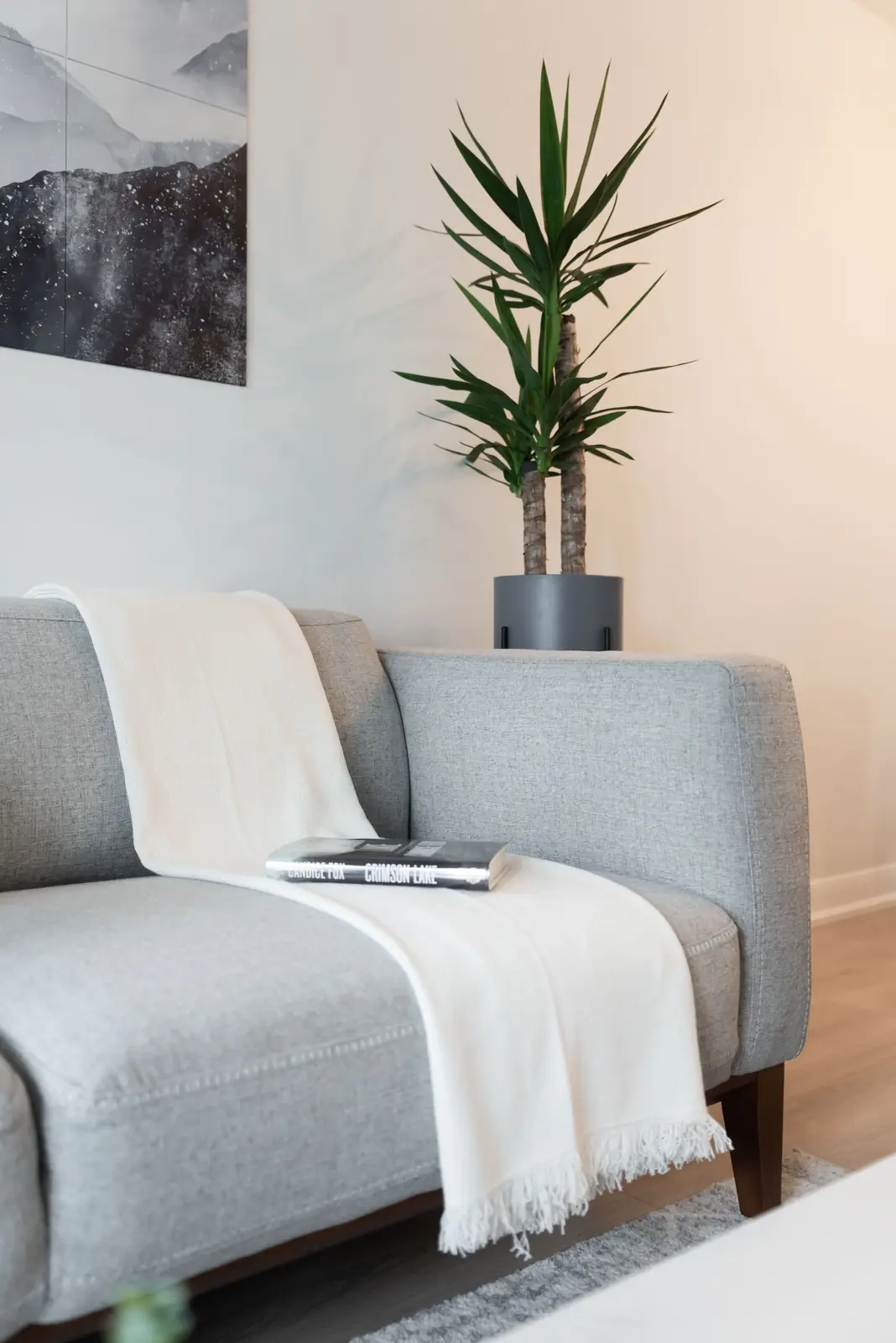Interior of a North York condo, with a pale sofa, a white kitchen, and light wood floors.