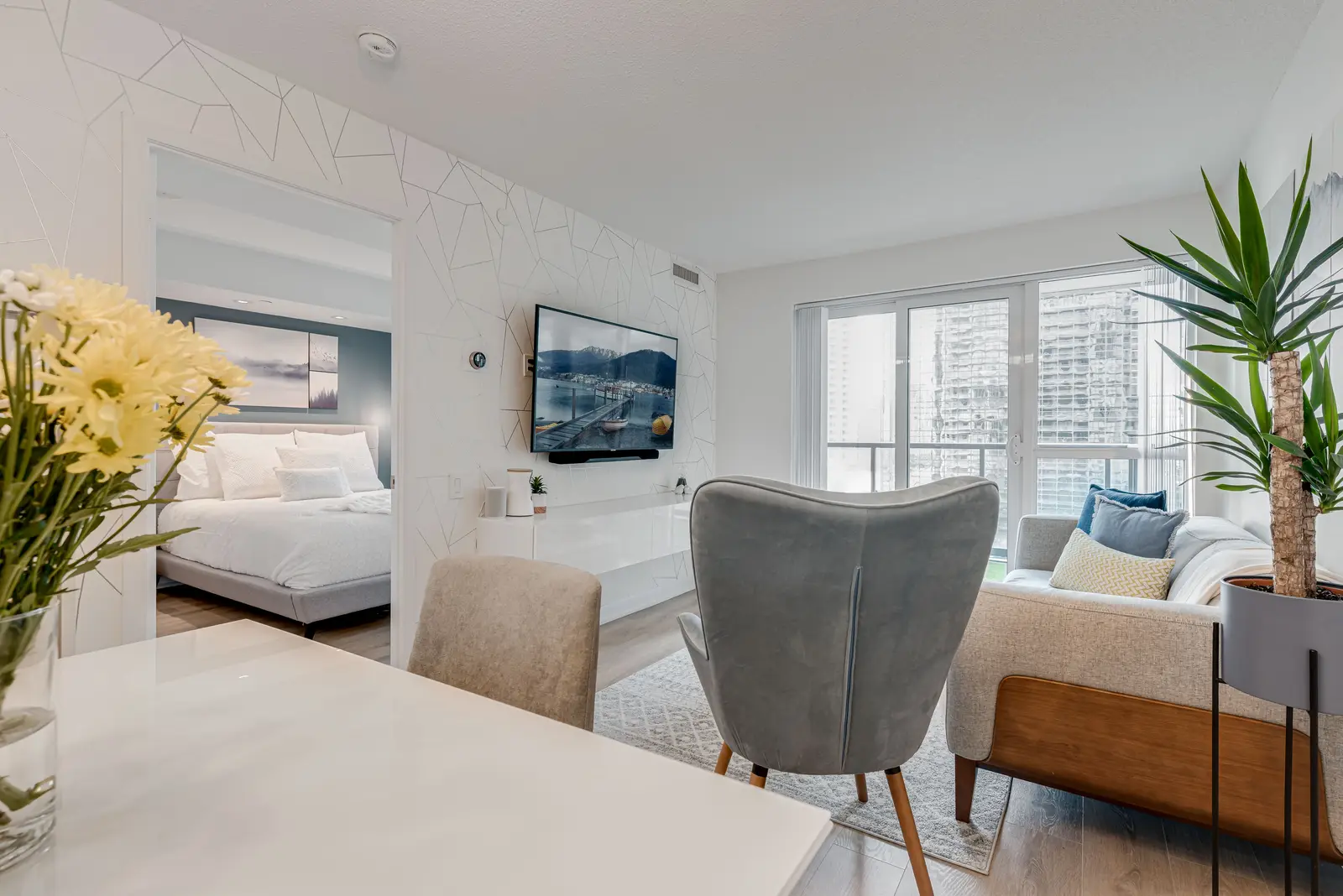 Interior of a North York condo, with a pale sofa, a white kitchen, and light wood floors.