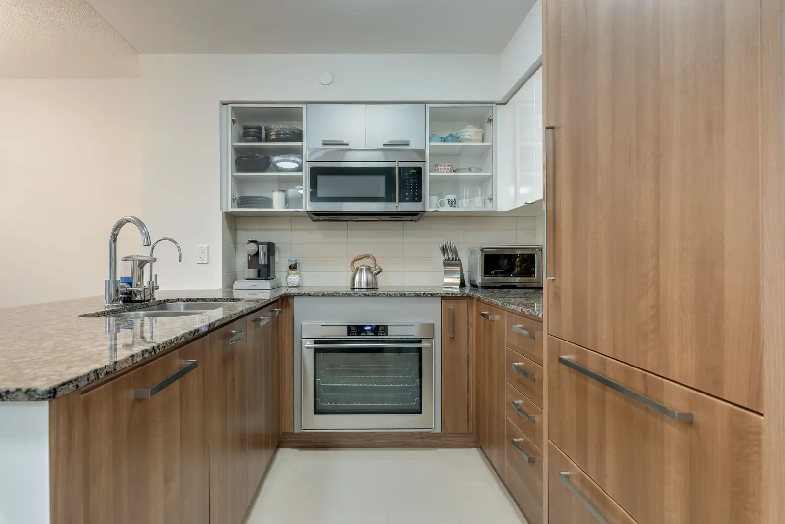 Interior of a North York condo, with a pale sofa, a white kitchen, and light wood floors.