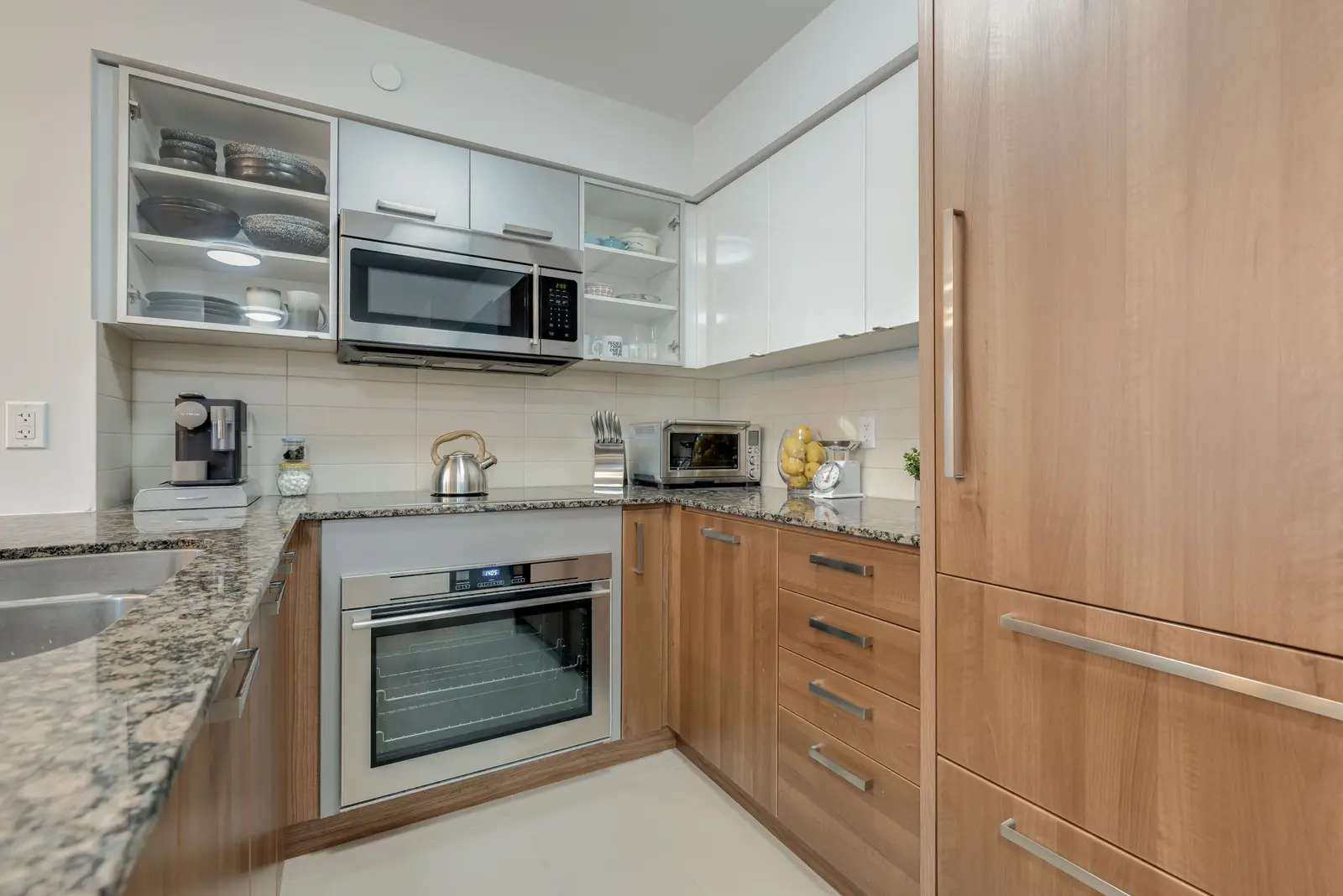 Interior of a North York condo, with a pale sofa, a white kitchen, and light wood floors.