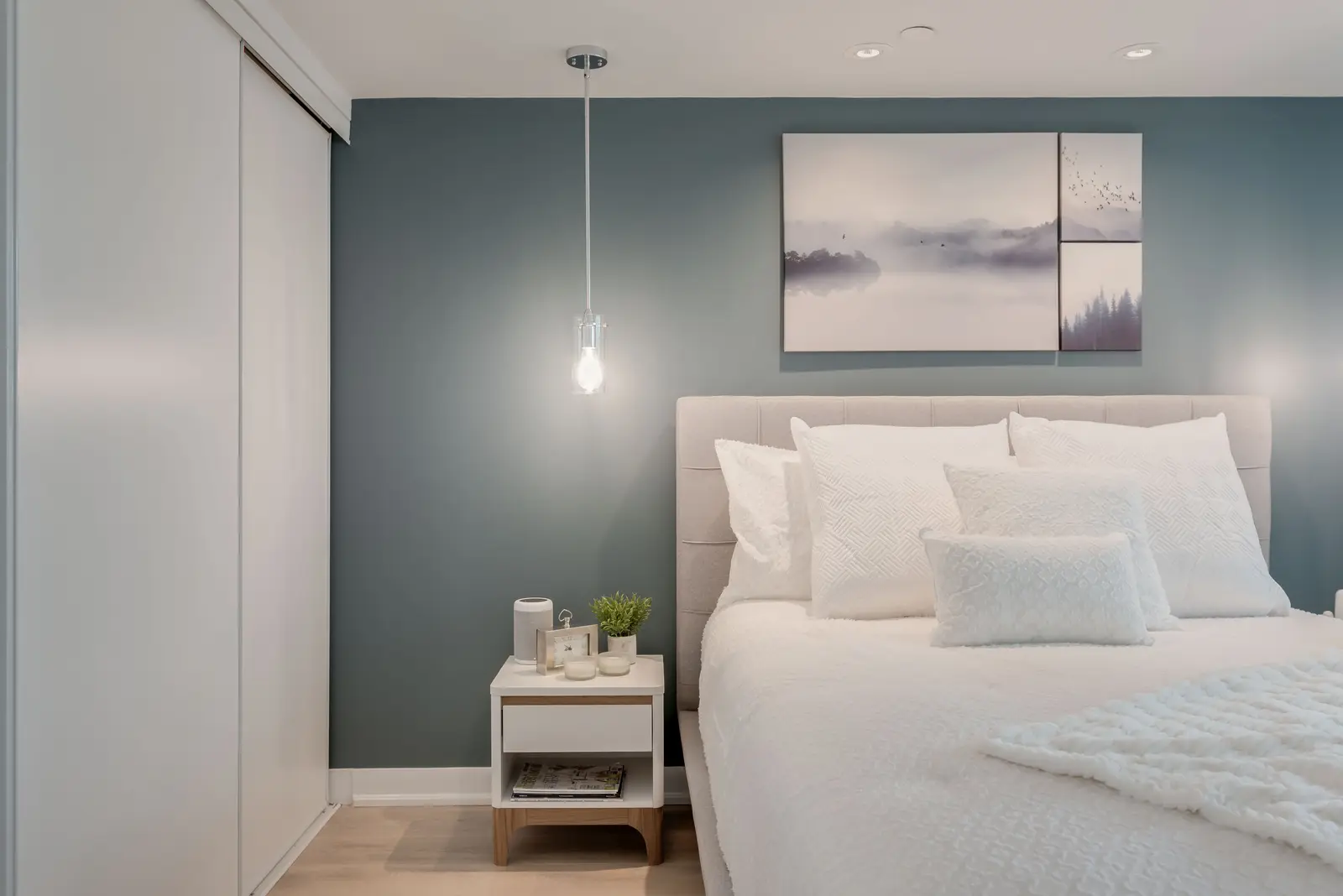 Interior of a North York condo, with a pale sofa, a white kitchen, and light wood floors.