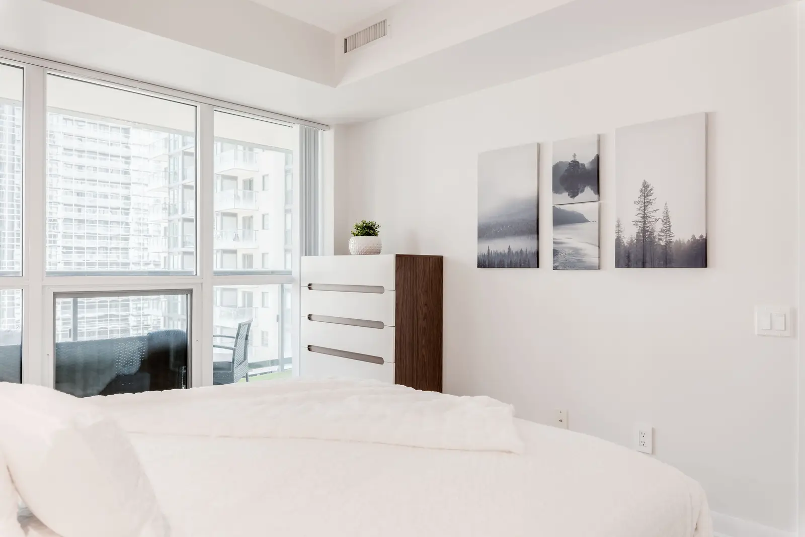 Interior of a North York condo, with a pale sofa, a white kitchen, and light wood floors.
