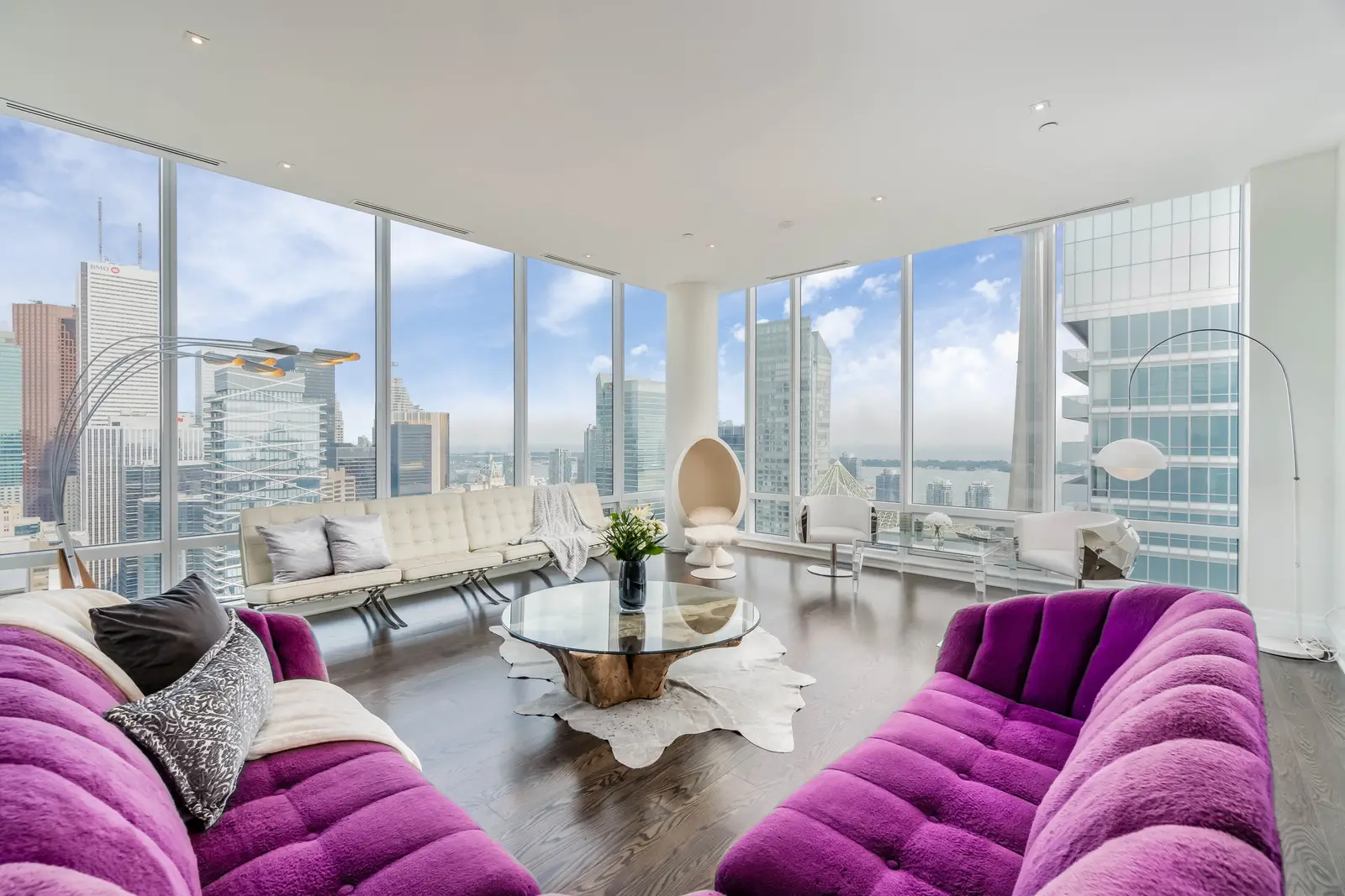 Interior of a condo on Adelaide Street West in Toronto, with purple chairs, a white living room, and the skyline beyond the glass.