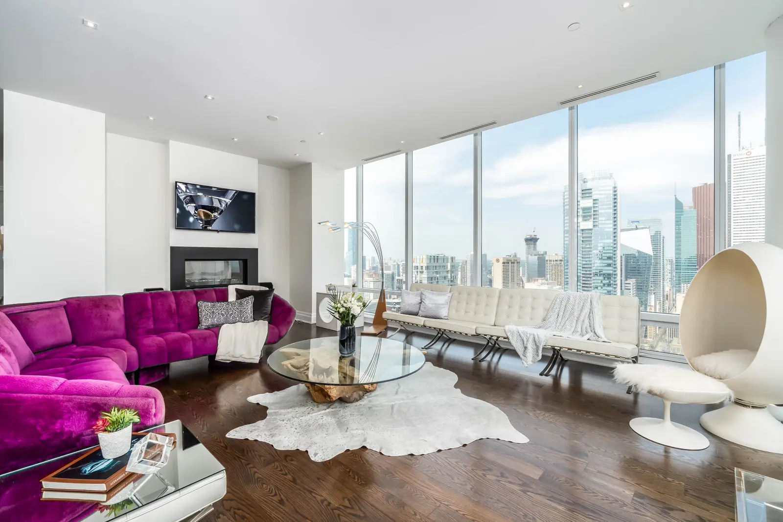 Interior of a condo on Adelaide Street West in Toronto, with purple chairs, a white living room, and the skyline beyond the glass.