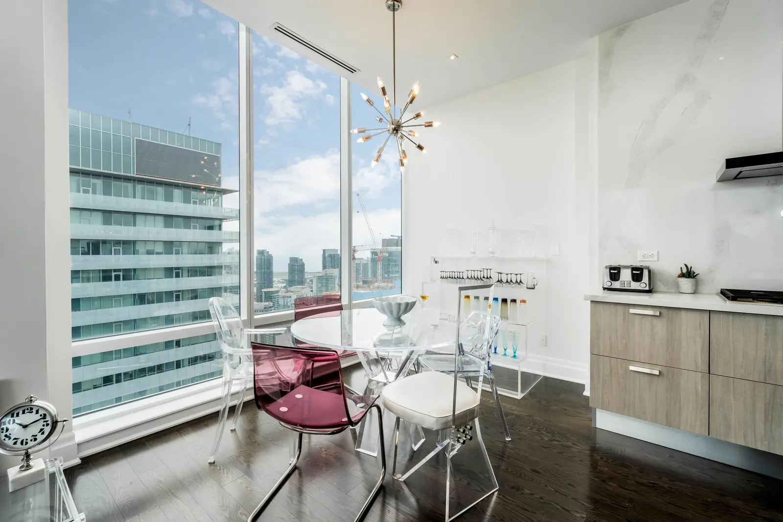 Interior of a condo on Adelaide Street West in Toronto, with purple chairs, a white living room, and the skyline beyond the glass.