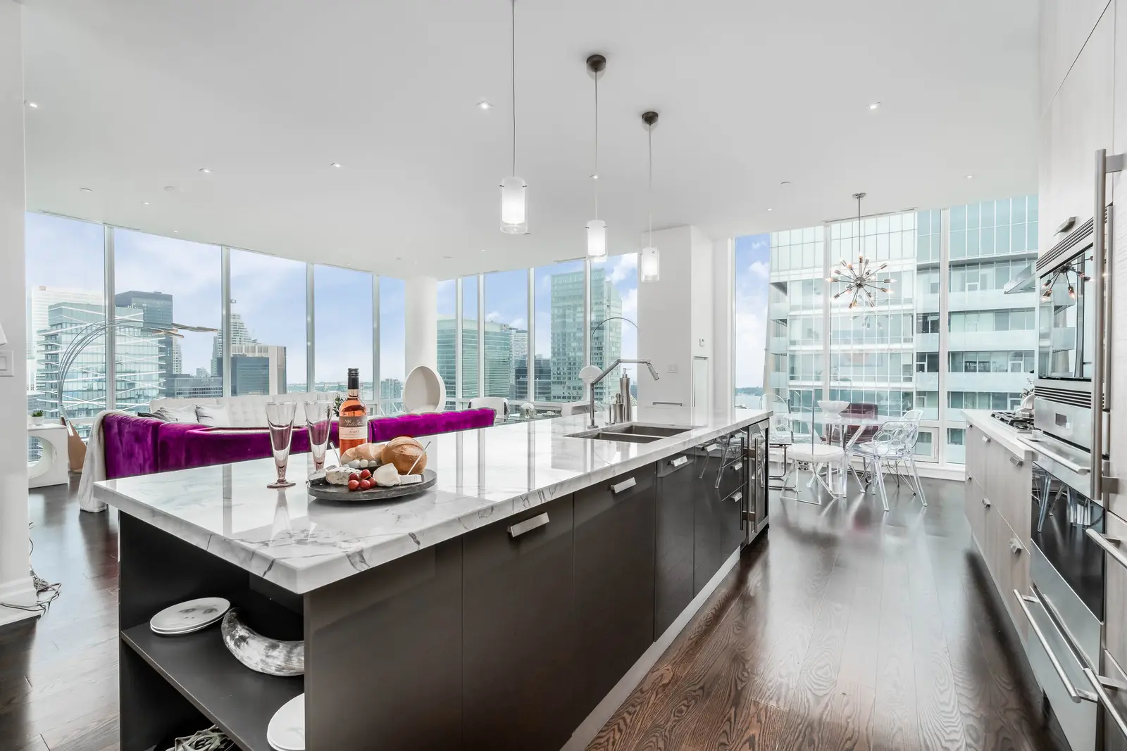 Interior of a condo on Adelaide Street West in Toronto, with purple chairs, a white living room, and the skyline beyond the glass.