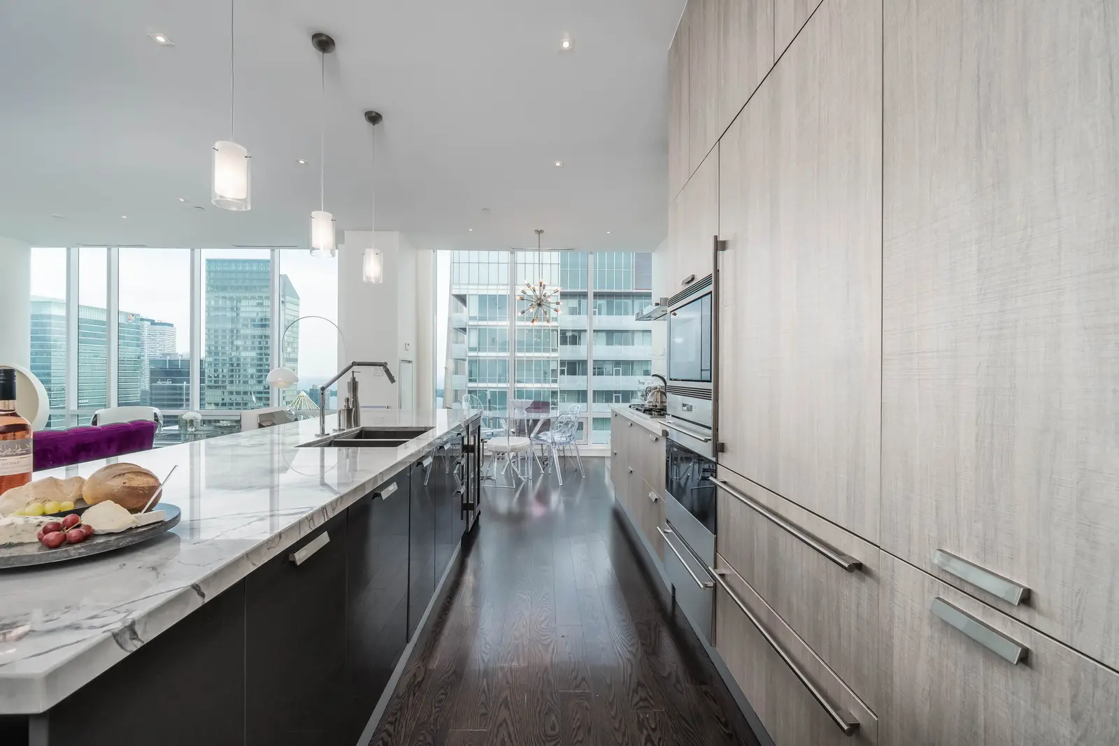 Interior of a condo on Adelaide Street West in Toronto, with purple chairs, a white living room, and the skyline beyond the glass.