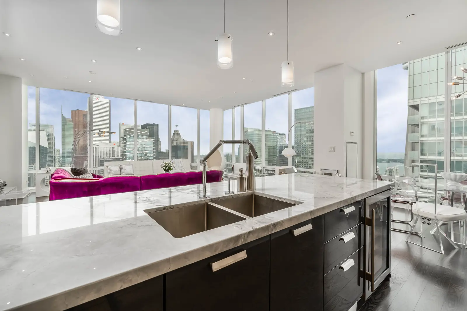 Interior of a condo on Adelaide Street West in Toronto, with purple chairs, a white living room, and the skyline beyond the glass.