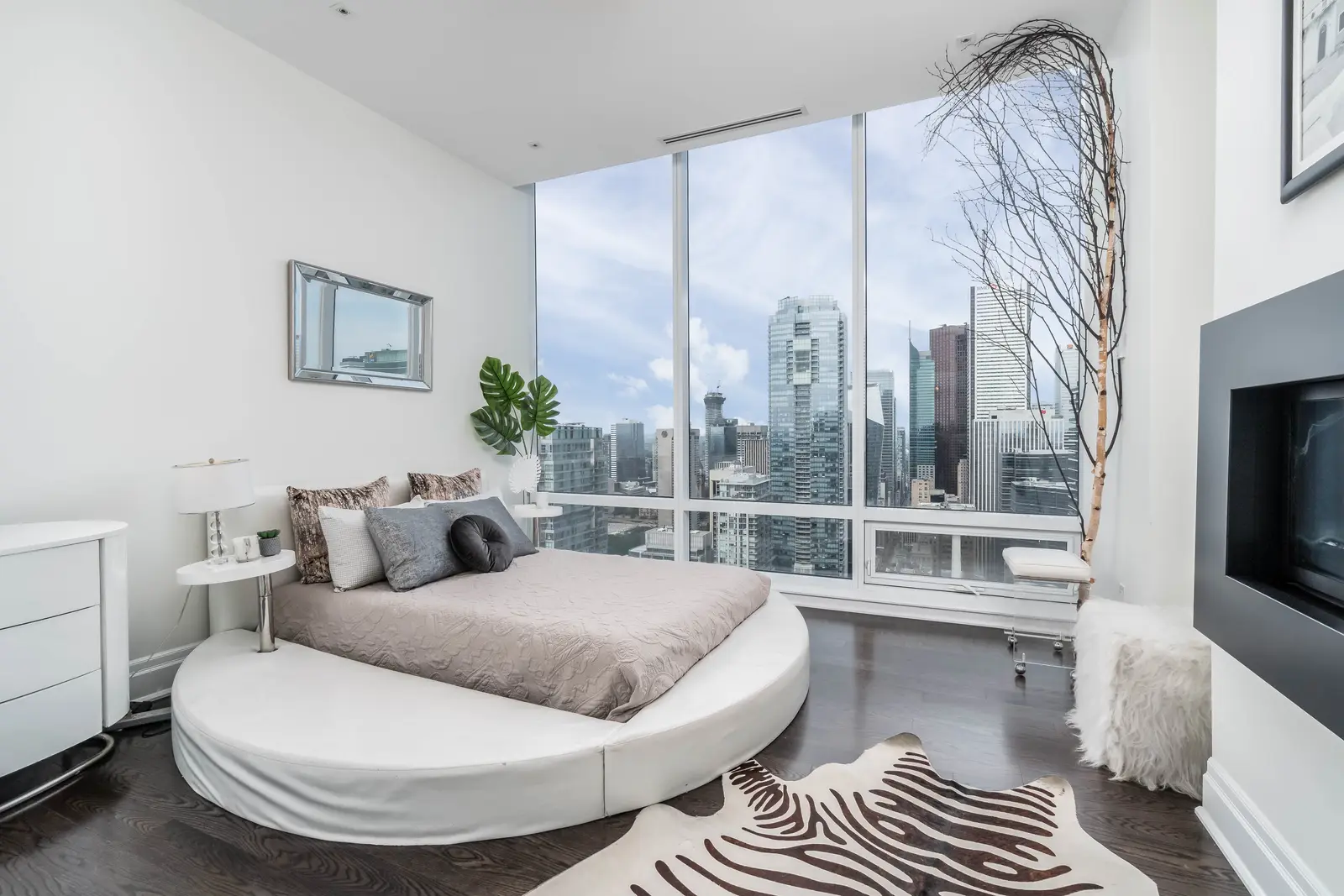 Interior of a condo on Adelaide Street West in Toronto, with purple chairs, a white living room, and the skyline beyond the glass.