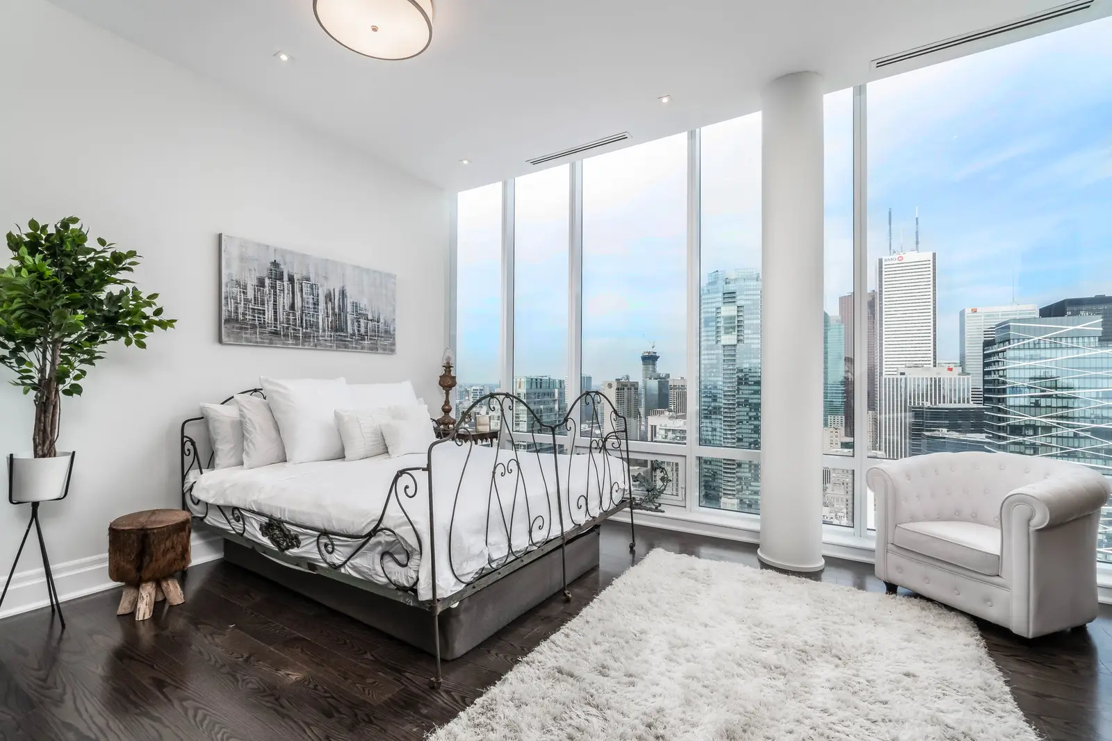 Interior of a condo on Adelaide Street West in Toronto, with purple chairs, a white living room, and the skyline beyond the glass.