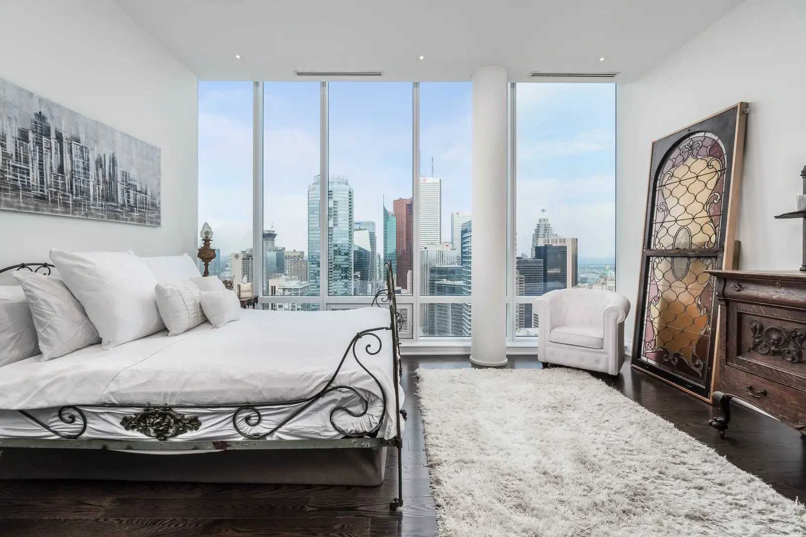 Interior of a condo on Adelaide Street West in Toronto, with purple chairs, a white living room, and the skyline beyond the glass.