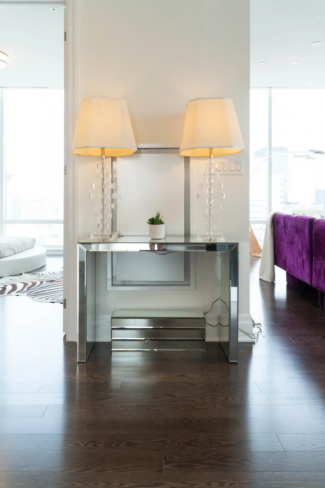 Interior of a condo on Adelaide Street West in Toronto, with purple chairs, a white living room, and the skyline beyond the glass.