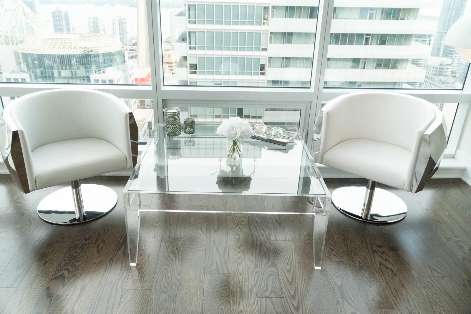 Interior of a condo on Adelaide Street West in Toronto, with purple chairs, a white living room, and the skyline beyond the glass.