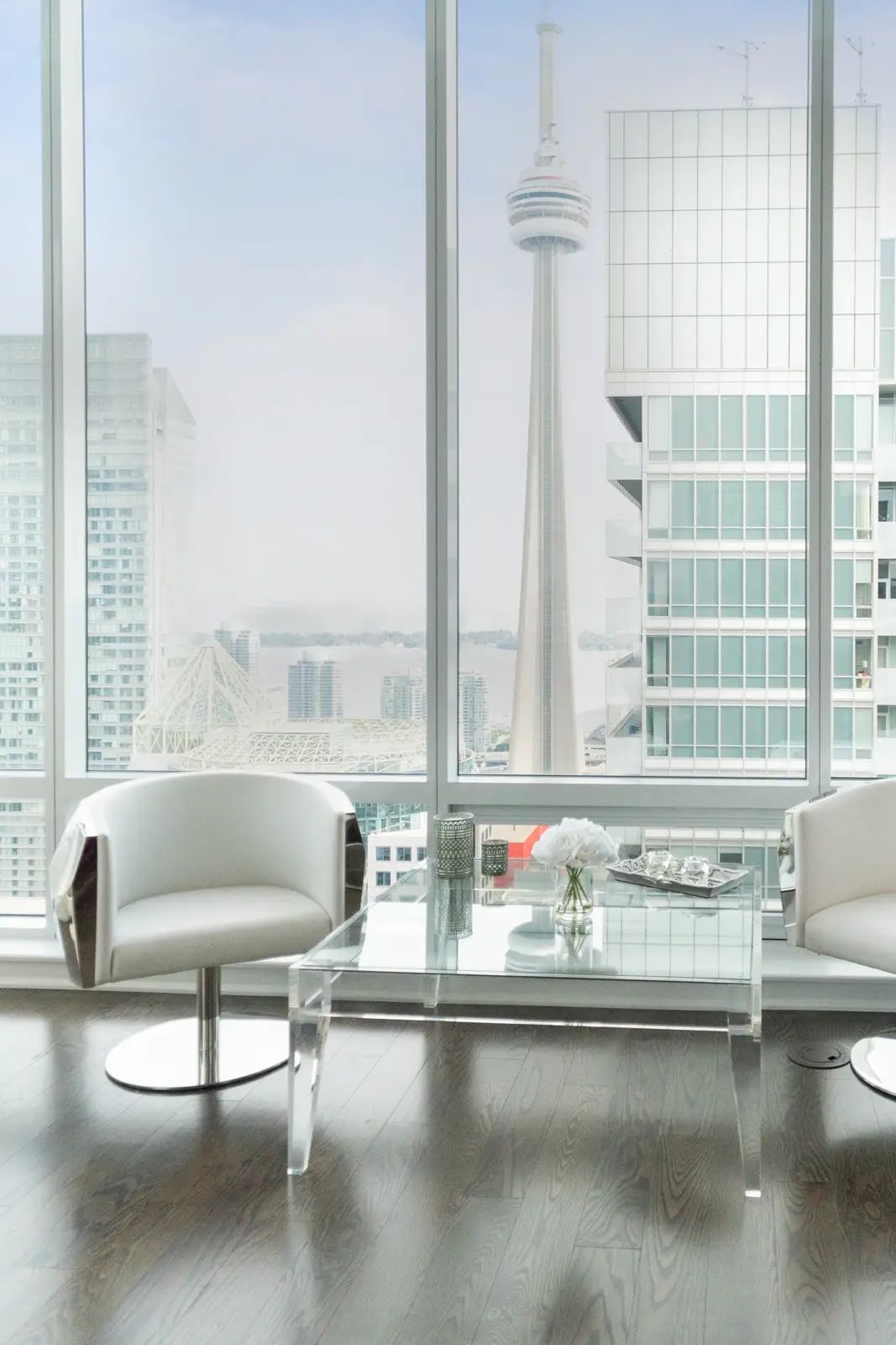 Interior of a condo on Adelaide Street West in Toronto, with purple chairs, a white living room, and the skyline beyond the glass.