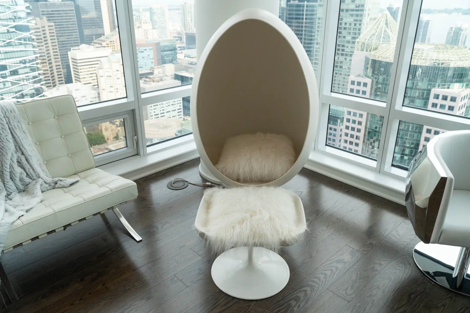 Interior of a condo on Adelaide Street West in Toronto, with purple chairs, a white living room, and the skyline beyond the glass.